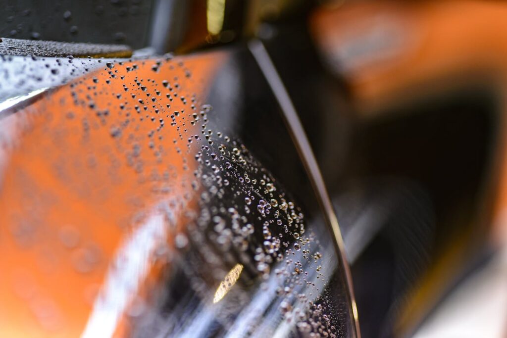 Close-up view of water droplets on a glossy car surface with a blurred background.