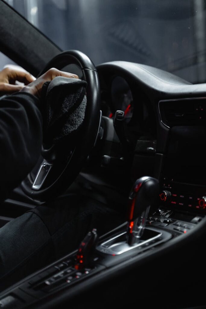 Close-up of a person cleaning a car's dashboard and steering wheel, focused on interior maintenance.